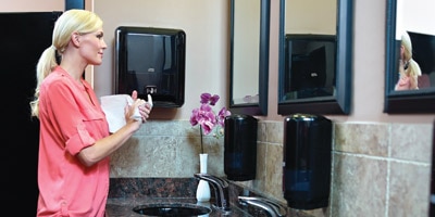 A woman in a bathroom drying her hands with a papel towel